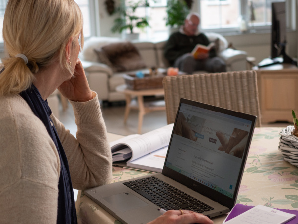 Brigitte werkt op haar laptop terwijl haar echtgenoot in de zetel zit